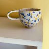 Splash keramikkop med hank fra Stenkvist Keramik. Koppen kommer i rustikt ler med orange og blå splash.