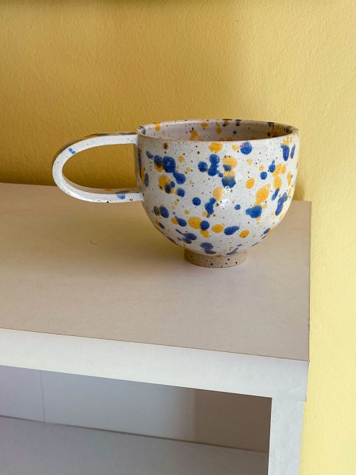 Splash keramikkop med hank fra Stenkvist Keramik. Koppen kommer i rustikt ler med orange og blå splash.